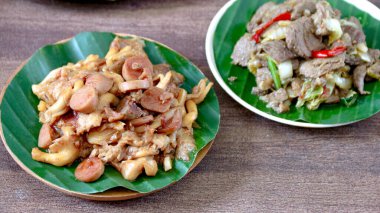 Muz yaprakları üzerinde sunulan farklı yemek tabaklarıyla dolu iki tabak ahşap bir yüzeye yerleştirilmiş, çeşitli mutfaklar için mükemmel..