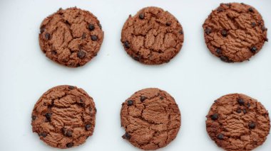 Altı taze çikolatalı kurabiye düz beyaz bir zeminde oturur. Atıştırmalık veya tatlı temalı tasarım projesi için mükemmeldir..