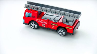 Genişletilebilir merdiveni parlak beyaz bir yüzey üzerinde sergilenen küçük kırmızı itfaiye aracı oyuncağı onu oyuncak fotoğrafçılık ya da çocukluk teması için mükemmel hale getiriyor..