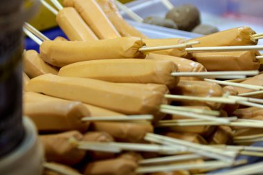 Ahşap çubuklarla delinmiş bir sosis yığını, sokak yemeklerini veya mutfak seçeneklerini sergilemek için mükemmel bir aperatif sunuyor..