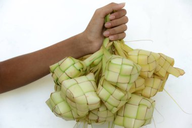 Ketupat olarak bilinen ve beyaz bir arkaplana karşı sergilenen bir avuç dokuma palmiye yaprağı kesesi, kültürel bir geleneği çağrıştırıyor ve yemekle ilgili içerikler için kullanılabilir..