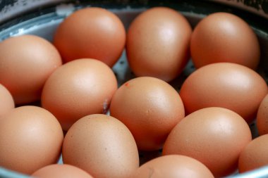 Gümüş bir sepetin içinde pişen kahverengi yumurtaların yakın plan çekimi. Pişirmeye ve yemeye hazır. Bu besleyici yemeğin tadını çıkarın..