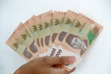 Bir el, finans ve ekonomi illüstrasyonları için kullanılan finansal kaynaklar ve zenginlik konseptini gösteren parlak bir geçmişe karşı bazı kağıt banknotlar tutuyor..