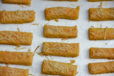 Fırında pişirilmiş peynir çubukları bir yemek tepsisinde sergilenir ve bir parti atıştırmalığı ya da ev yapımı ikramlar için mükemmeldir..