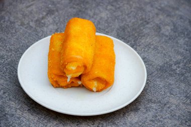 Peynirle doldurulmuş üç kızarmış börek gri bir arka plana karşı beyaz bir tabakta istiflenir, yemek fotoğrafçılığı veya menü tasarımı için idealdir..