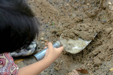 Bir çocuğun eli, dışarıda toprağı eşeleyen bir kürek tutar, oyun ve keşifle meşgul olur. Çocukluk eğlencesi ve açık hava aktivitelerini göstermek için birebir..