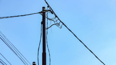 Karmaşık siyah kabloları gösteren karanlık elektrik direği durgun, yumuşak, mavi bir gökyüzüne karşı duruyor, endüstriyel basitlik hissi yaratıyor, telekomünikasyon veya altyapı pazarlaması için ideal..