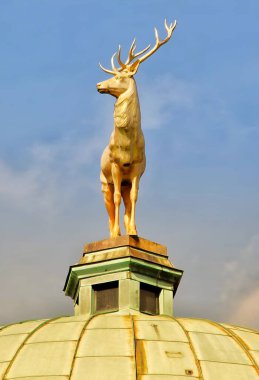 Altın bir geyik heykeli, mimari bir kubbenin önemli bir simgesidir. Açık, güneşli hava ve arka plandaki parlak mavi gökyüzü altın boynuzları ve ayrıntıları parlatıyor..