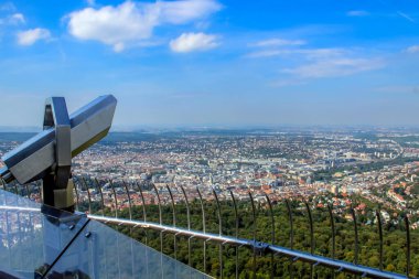 Stuttgart şehrine ve bir gözlem güvertesinden alınan çevreye geniş bir bakış açısı. Ön planda, metalik bir teleskop mavi bir gökyüzünün altında geniş şehir manzarasına bakıyor..