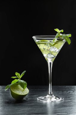 Yaz taze kokteyl limon dilimleri, ezilmiş buz ve nane ile bir martini cam arkadan aydınlatmalı siyah arka plan üzerine bırakır.