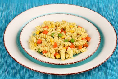 Fesleğen pesto, havuç, Mısır ve bezelye turkuaz mavi peçeteye bir plaka ile lezzetli ev yapımı Düdük makarna pişmiş