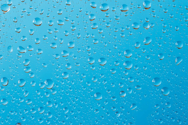 Macro shot of water drops with reflections on a window glass against turquoise blue background