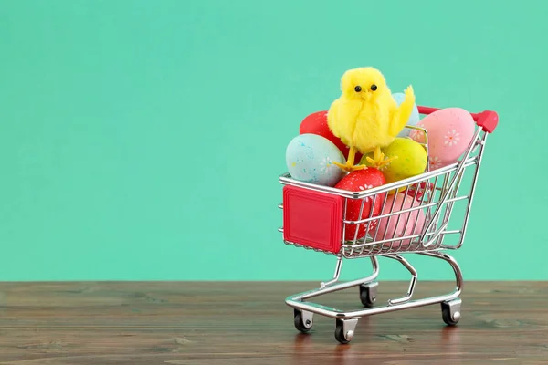 Galinha decorativa bonito em uma pilha de ovos pintados coloridos em um carrinho de compras contra fundo turquesa com espaço de cópia. Conceito de Páscoa — Fotografia de Stock