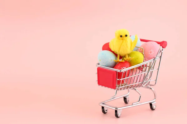 Galinha decorativa bonito em uma pilha de ovos pintados coloridos em um carrinho de compras contra fundo rosa com um espaço de cópia. Conceito de Páscoa — Fotografia de Stock