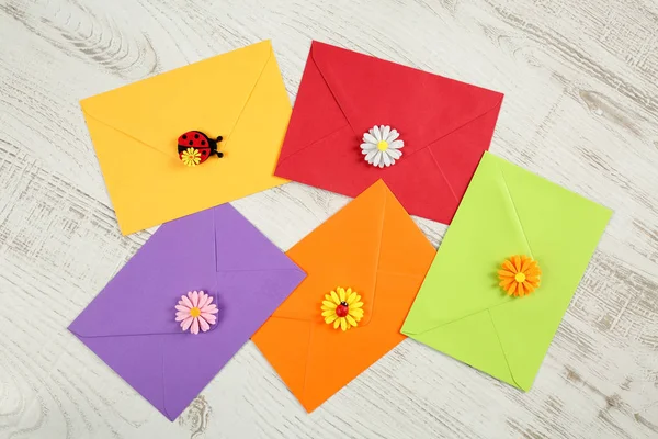 Ovanifrån av fem färgglada kuvert från återvunnet papper med dekorativ blomma kronblad och nyckelpigor på vit trä bakgrund. Hej våren sommaren koncept — Stockfoto