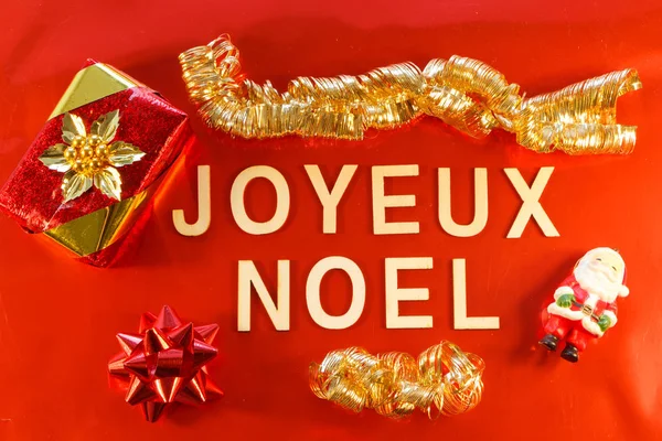 Merry Christmas written in french language with gift and Christmas decorations on red background
