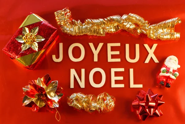 Merry Christmas written in french language with gift and Christmas decorations on red background