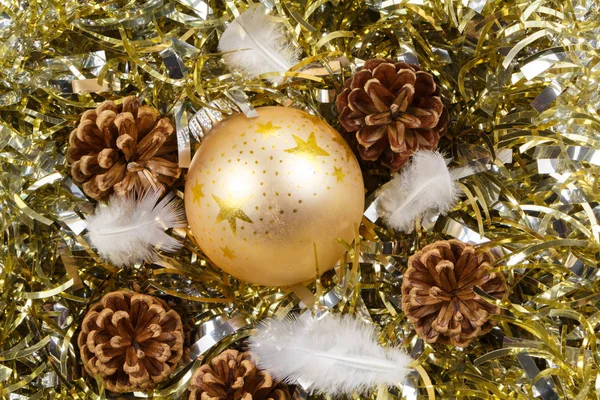 Çam konileri, tüy ve altın bir tinse üzerinde altın Noel topu — Stok fotoğraf