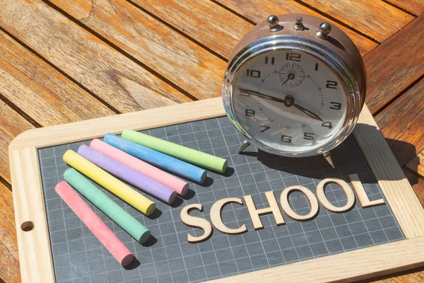 Alarm clock, chalks and chalkboard slate with school written in wooden letters