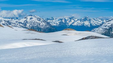 A serene panorama unfolds across Kenai Fjords National Park, Alaska, where snow-capped mountains meet a tranquil blue sky.