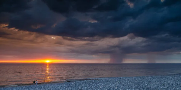 人们在日落海滩和雷暴乌云在海上 — 图库照片