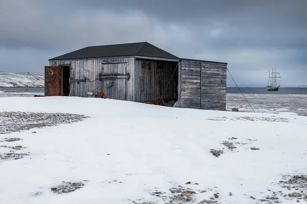 斯匹次卑尔根被雪覆盖的海岸上的废弃房屋和海上船只 — 图库照片