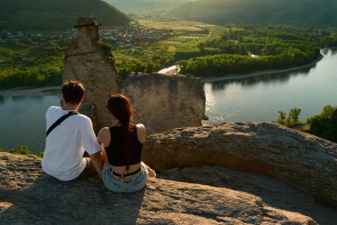 Günbatımında ortaçağ şatosu harabelerinde oturan çift, güneşli Vachau Vadisi 'ne, geniş Tuna Nehri' ne ve üzüm bağlarına bakarak Avusturya 'da romantik ve manzaralı manzaralar yaratıyor..