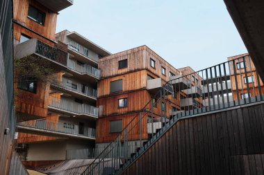 Viyana 'daki modern çok katlı apartman binasında gri bir gökyüzünün altında beton Bauhaus tarzı balkonlar, ahşap kahverengi ön cephe panelleri yer alıyor..