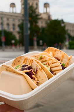 Beyaz bir sokak yiyecek kutusunda servis edilen üç taco, şehir yüzeyinde canlı şehir atmosferini ve günlük yemek atmosferini yakalıyor..