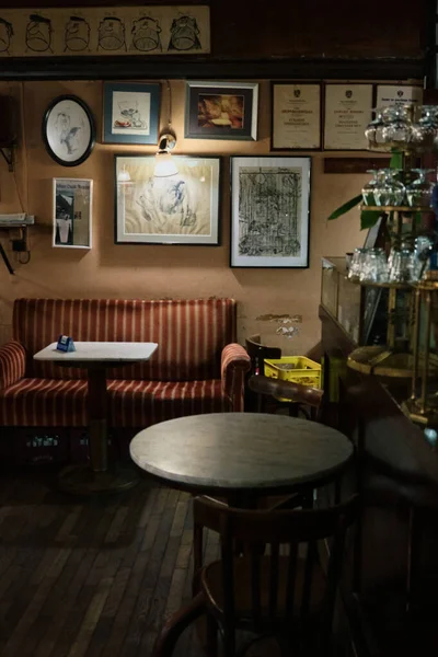 Sayısız tablonun bulunduğu tarihi bir kafe köşesinin içi, yan tarafında bardaklar olan bir bar, hafif ışıklandırma, sandalyeli küçük bir masa ve çizgili bir kanepe..