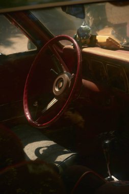 Parlak kırmızı direksiyona yakın çekim ve siyah vitesli kırmızı arabanın içi. Dikiz aynasında mini disko topu, güneş ışığıyla yıkanmış..