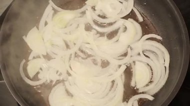 Kızartma tavasında sıcak ayçiçeği yağında cızırdayan dilimlenmiş soğan halkalarının yukarıdan görünüşü. Minimalist parlak mutfak sahnesi yemek pişirme sürecini karıştırmadan yakalıyor..