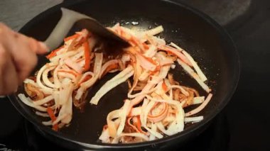 Karamelli soğan, yengeç çubuğu, sarımsak tozu ve biberli tavanın üst görüntüsü. Kadın eli her şeyi bir spatulayla karıştırır. Parlak mutfak aşçılık sahnesi.