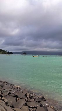 Turkuaz denizde yüzen balıkçı tekneleri ve dramatik fırtına bulutları. Sahil yaşamının manzarası ve geleneksel deniz manzarası. Blitar, Endonezya. 12 Mayıs 2023