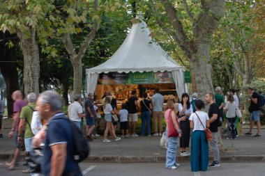 White market tent with crowds of visitors at Cheese 2025 Slow Food festival in Bra's tree-lined street. The biennial international cheese event attracts food enthusiasts to sample artisanal dairy products.
