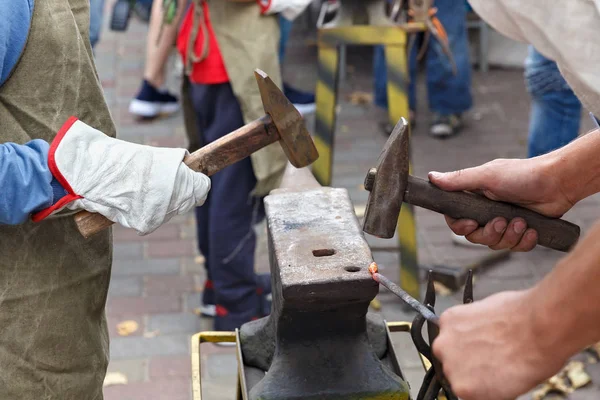 Work with hammers on the anvil in the street forge workshop.