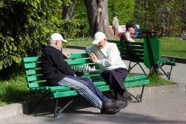 Central Park 'ta yeşil ahşap bankta satranç oynayan iki bilinmez yaşlı erkek.