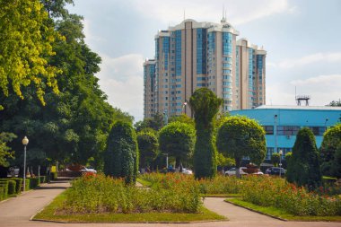 Arka planda modern yüksek katlı konut binaları ile Almatı Şehir Parkı görünümü. 