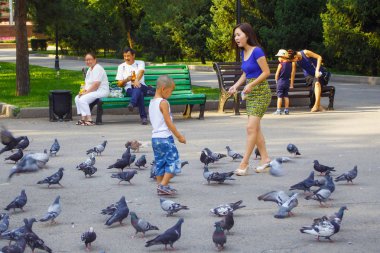 Unknown people feeding pigeons in 28 Panfilov city park in Almaty.