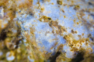 Sığ bir alan derinliği etkisi ile makro modda fotoğraflanan renkli taşın ıslak yüzeyinin bulanık dokusu.