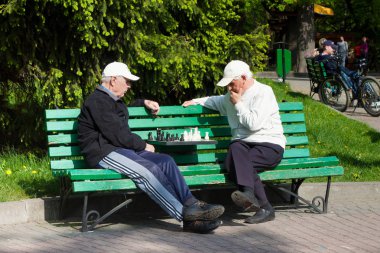 Central Park 'ta yeşil ahşap bankta satranç oynayan iki bilinmez yaşlı erkek.