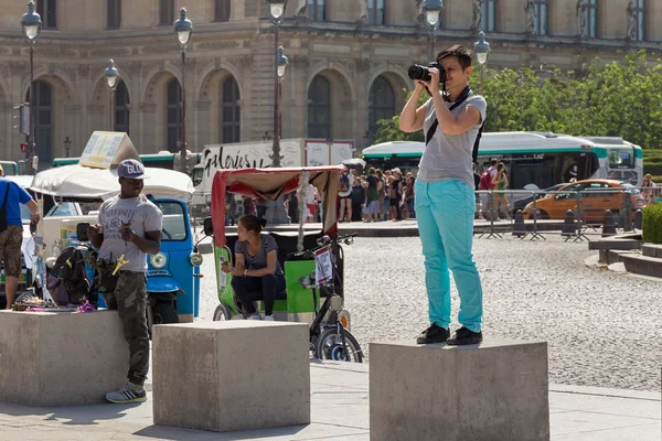 Unknown young woman standing on the concrete cube and taking a photo of the famous Louvre Palace — Stock Photo, Image