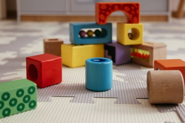 Çocukların oyun hasırına saçılmış renkli ahşap öğrenme blokları yaratıcılığı ve problem çözmeyi teşvik ediyor..