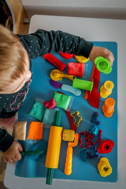 Çocuklar yaratıcı dokunmatik oyunlar için hamur silindirleri, parlak kesiciler ve renkli araçlar kullanırlar..
