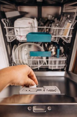 Temizlik döngüsüne başlamadan önce bulaşık makinesine deterjan koyan birinin yakın çekimi. Ev işleri ve modern ev aletleri konsepti.