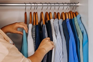 Close up of a hand selecting clothes from a neatly organized wardrobe with wooden hangers. Concept of fashion choice and lifestyle.