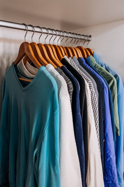 Wardrobe with colorful shirts and sweaters neatly organized on wooden hangers. Concept of order, style, and fashion.