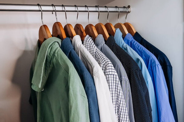 Row of colorful mens shirts hanging on wooden hangers inside a wardrobe, showing organized clothing and smart casual style. 