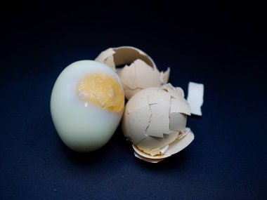 Kabuğu soyulmuş katı yumurta ve kırık kahverengi kabuk parçaları, koyu arka planda izole edilmiş, beslenme ve kahvaltı temaları için mükemmel.