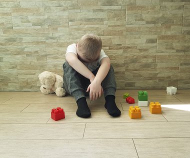  katta oturan bir oyuncak ayı ile üzgün küçük çocuk